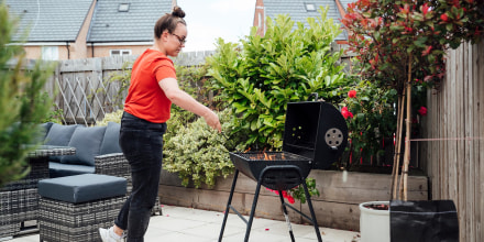 Woman standing over a charcoal grill, grilling. Shop the best charcoal for grilling to use with your charcoal grill. The best grilling charcoal and charcoal tools are from Weber, Royal Oak, Rockwood and more.