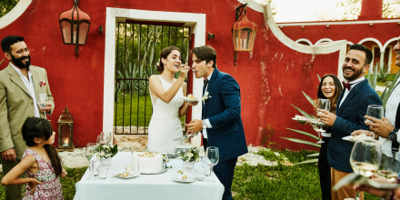 Laughing bride feeding cake to groom during outdoor wedding reception. These are the best wedding cake toppers to try in 2021. Shop custom and unique wedding cake toppers from Etsy, Hobby Lobby, Michaels and more.