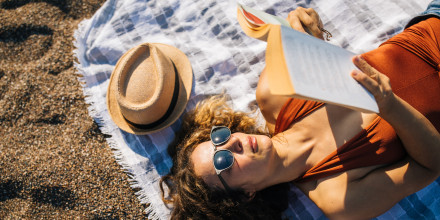 Woman lies on the beach reading a book
