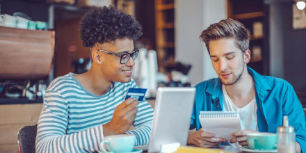 Young men working at home office, holding up a credit card