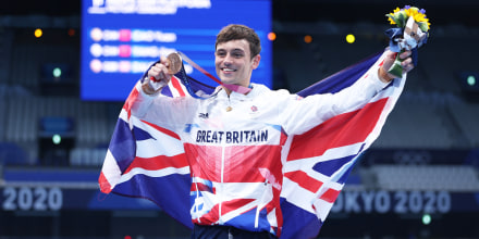 Tom Daley wears the flag of great britain and poses with his medal, smiling