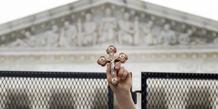 Image: A hand holding a cross outside the Supreme Court
