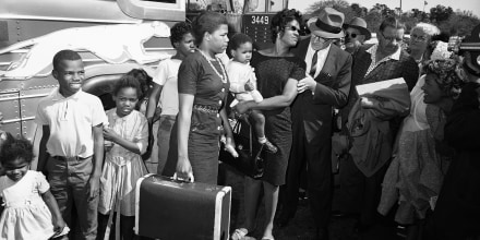Victoria Bell, wearing glasses, holding infant, is greeted by Selectman E. Thomas Murphy on arrival from Little Rock., Ark