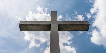 A Large Concrete Cross On A Cemetery Against A Blue Sky With White Clouds.
