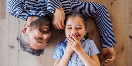 Top view of mature father and small daughter lying on floor indoors at home.