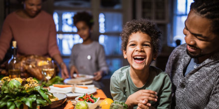 little boy laughing while at the dinner table in his father's arms 