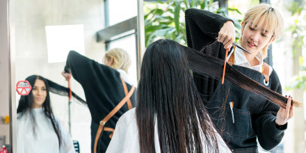 Female barber combing and adjusting customer hair during haircut in barber shop or beauty salon.