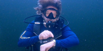 In this photo provided by the Florida Keys News Bureau, diving explorer and medical researcher Dr. Joseph Dituri points to his watch Friday, June 9, 2023, indicating that it is time to surface after spending 100 days in the Jules' Undersea Lodge marine habitat at the bottom of a Key Largo, Fla., lagoon. Dituri broke the previous 73-day record for underwater human habitation at ambient pressure, undertook medical and marine science research and interacted online with more than 5,500 students during his Project Neptune 100 mission organized by the Marine Resources Development Foundation. (Mariano Lorde/Florida Keys News Bureau via AP)