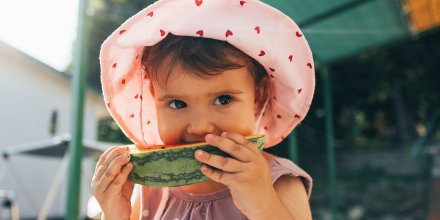 A Cute Baby Girl Eating Watermelon While Standing Outdoors