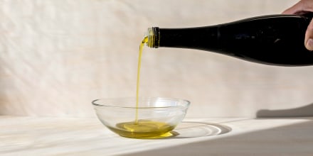 A hand pouring olive oil from a bottle into a small glass bowl.