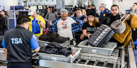 People place their items into bins in line at the airport with TSA