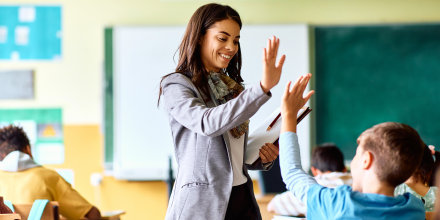 Happy school teacher giving high-five to her student during class.