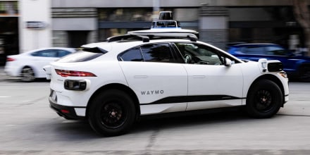 A white Waymo robotaxi vehicle driving on the street