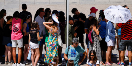 People queue under a shade.