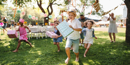 Small children running with presents outdoors at a birthday party.