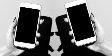 Womens hands holding two iPhones with dark shadows cast behind them.