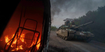 A Ukrainian tank passes by a burning car near the Russian-Ukrainian border on August 14, 2024.