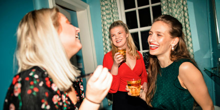 Three young women are applying makeup with a drink in the bathroom at a house party.