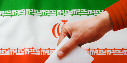 A person dropping a ballot into a box with the Iranian flag behind them.