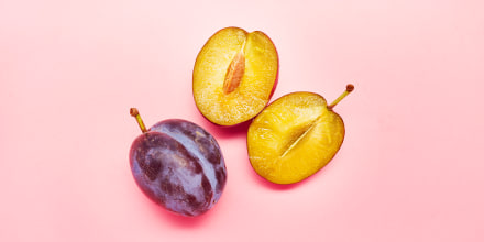 Still life of sliced plums on pink background.