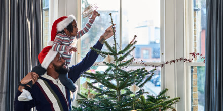 Girl on father's shoulders putting star on top of Christmas tree