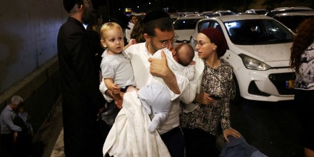 A man holds children as people take cover during an air raid siren, in central Israel