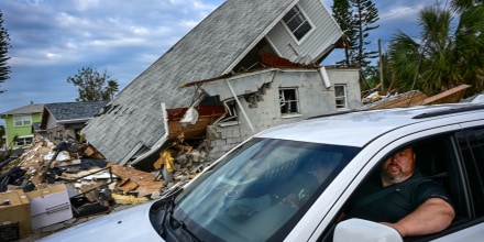 A person in a car drives past a destroyed home