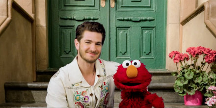 Andrew Garfield and Elmo sit on a stoop