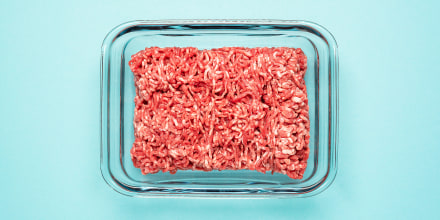 Above view of raw ground beef in a glass food container on a blue colored table.