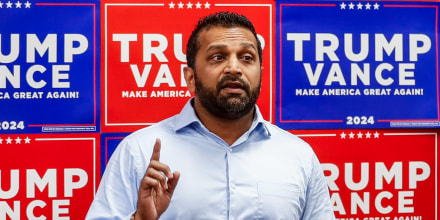 Kash Patel speaks, red and blue Trump Vance signs line the wall behind him