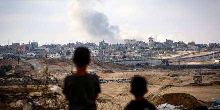 Young boys look at billowing smoke against a city skyline.