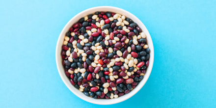Mix of raw beans in a white bowl on a blue background. Top view and copy space.