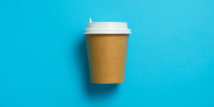 Disposable paper cup with lid for coffee on a bright pastel blue background.
