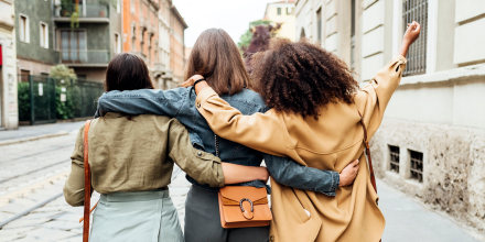 Three woman walking in the city with arm around each other.