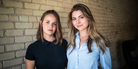 Lea Burbidge Izquierdo, left, and Francesca Albo stand next to each other in front of a beige brick wall