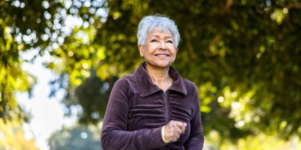 Senior woman running on a beautiful day outdoors under trees