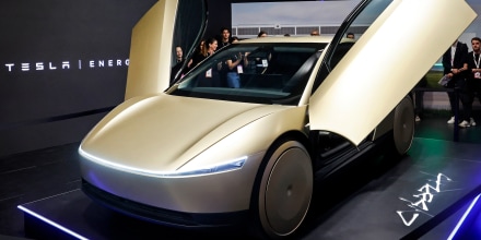 A Tesla Robotaxi vehicle, painted gold, inside of a showroom