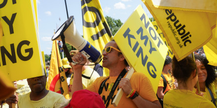 People protest holding yellow signs that say "Not My King"