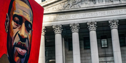 A poster of a painting of George Floyd is held up near a building exterior outside