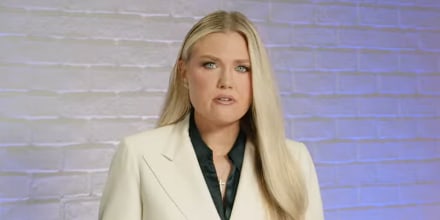 Erika Kirk stands at a podium and speaks, the podium has text that reads "May Charlie be received into the merciful arms of Jesus, our loving Savior" above a photo of Charlie Kirk's face