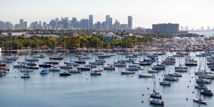 A drone view shows sailboats moored next to the Coconut Grove Sailing Club and the downtown skyline in Miami