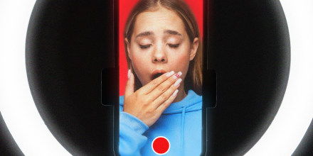 A girl yawning on a phone screen with a record button, surrounded by a ring light.