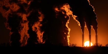 Silhouettes of large billowing smoke coming out of smoke stacks as the sun sets