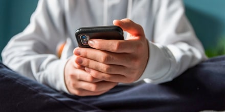 Close up of hands of teen boy in white sweater texting on phone.