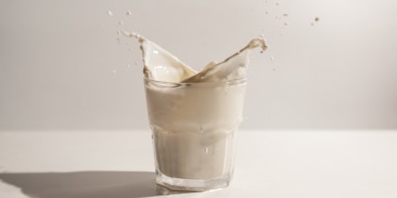 Splash of milk from the glass on a white table, dairy concept