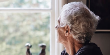 Image: Senior man looking through window while sitting at home