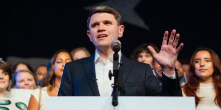 James Talarico speaks at a podium in front of people holding signs that say "Talarico for Texas"