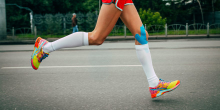 Image: A girl athlete running with her knees in blue kinesiology taping 
