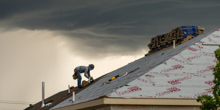 Roofing construction worker installing shingles in thunderstorm