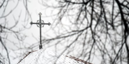 A cross sits atop a building at the Archdiocese of Denver, shrouded by branches